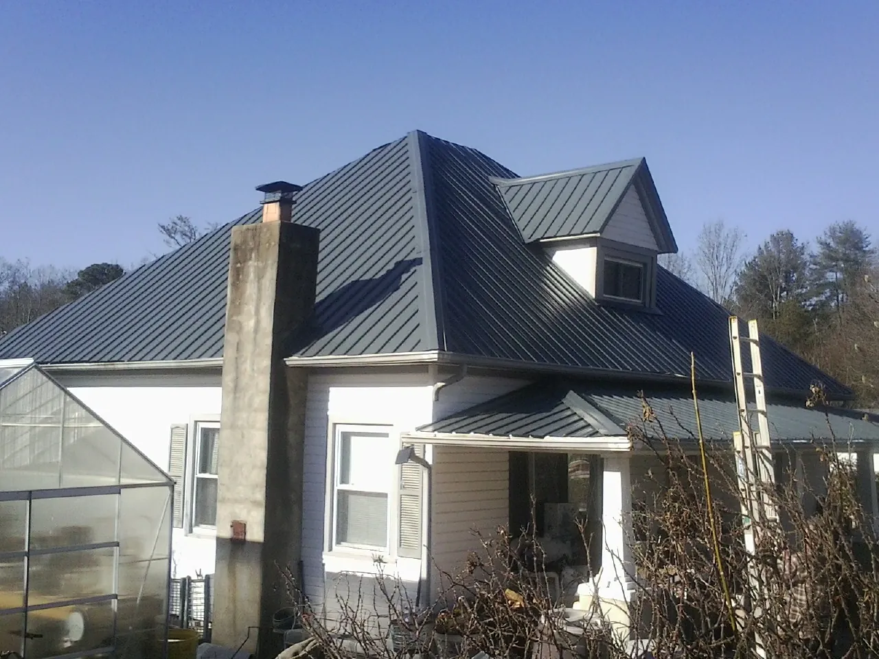 Dark blue standing seam metal roof on a white farmhouse with dormer — Slate & Tile Roof Repair by Roofing Brothers in Cortlandt Manor