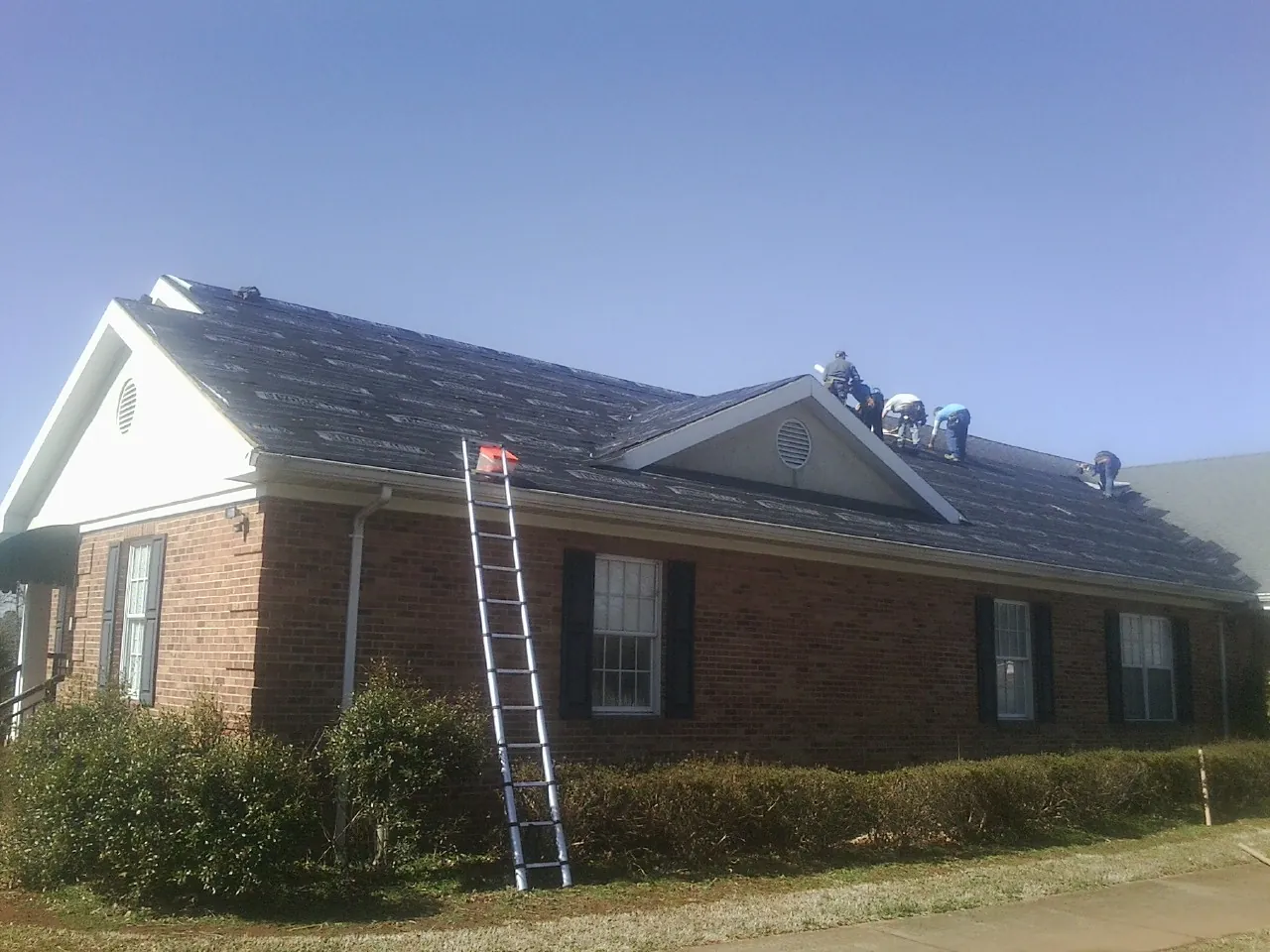 Crew tearing shingles off a brick ranch roof with a ladder set — Metal Roof Repair work by our crew in Cortlandt Manor