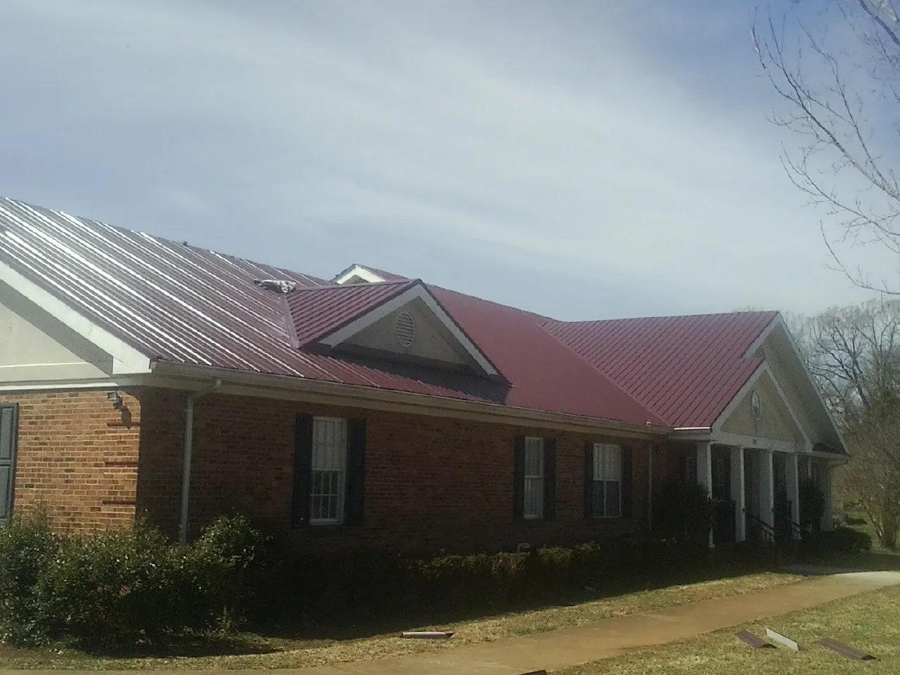 Red metal roof with gabled entries on a long brick building, from a Hail Damage Roof Repair job in Cortlandt Manor