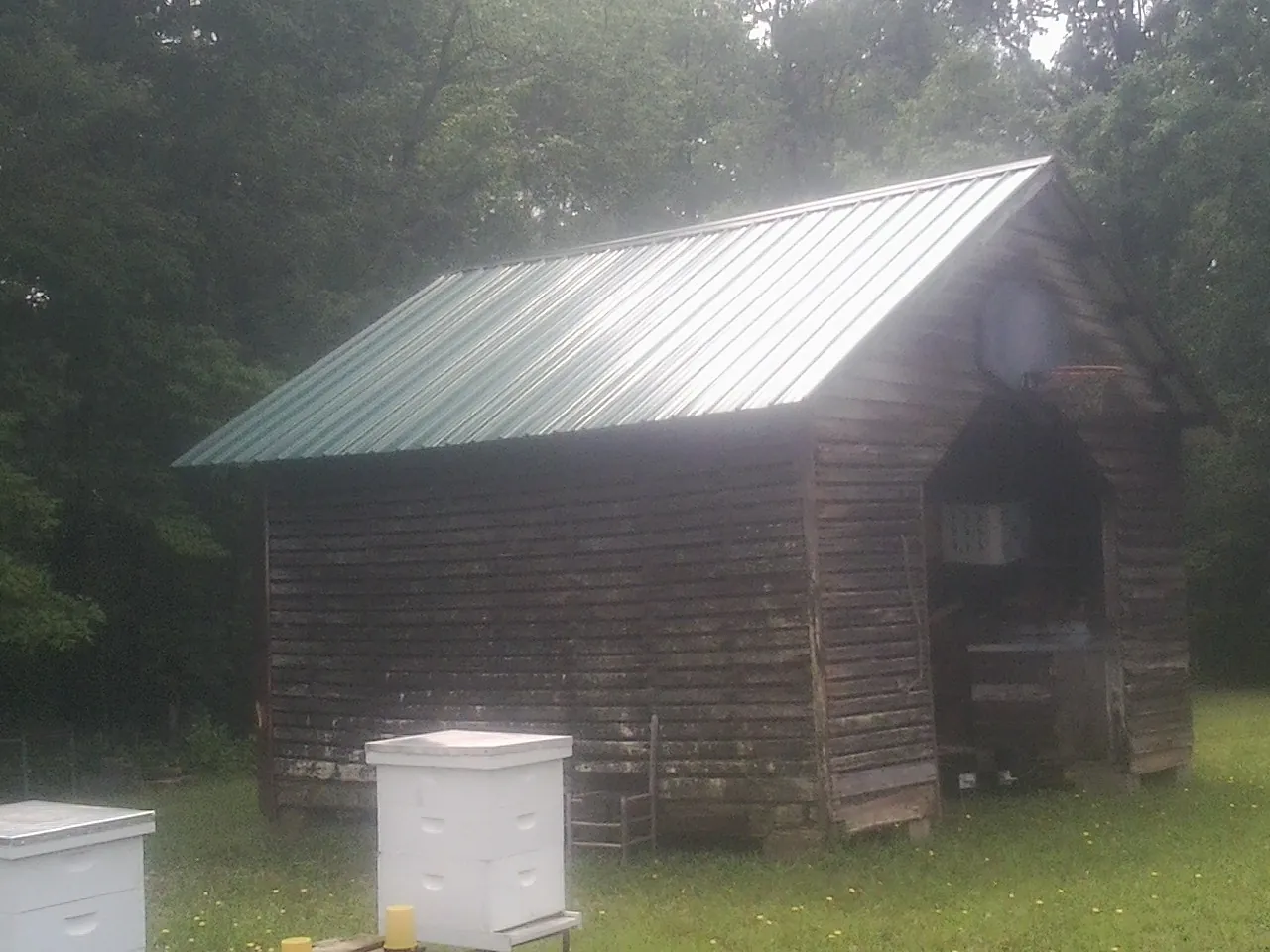 Green metal roof on a weathered barn beside stacked beehives in Cortlandt Manor