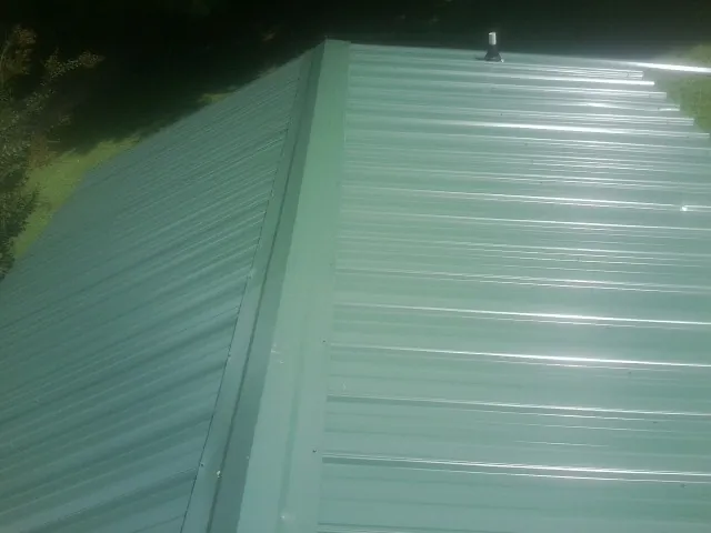 New green metal panels meeting at the ridge of a roof — Flat Roof Repair work by our crew in Cortlandt Manor