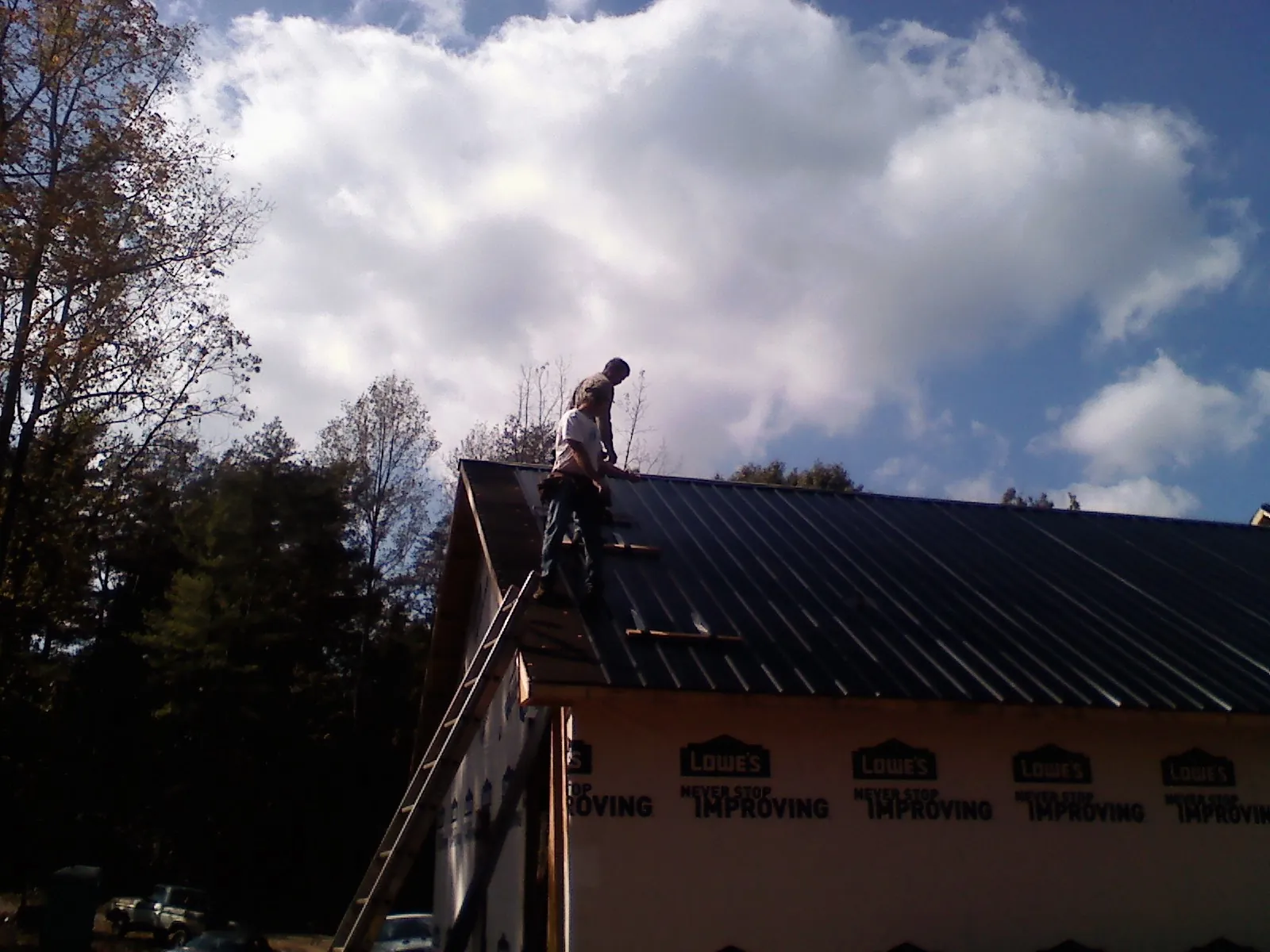 Roofer fastening dark metal panels high against a cloudy sky, from a Roof Inspection job in Cortlandt Manor