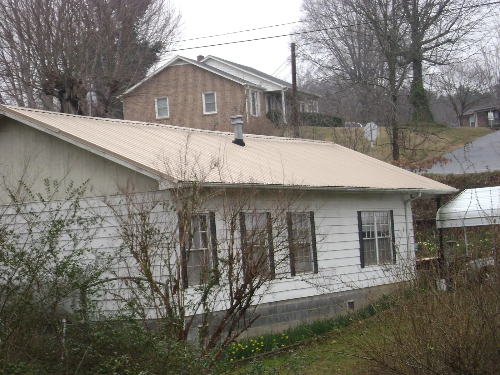 Tan metal roof on a white sided house set into a hillside — Commercial Roofing by Roofing Brothers in Cortlandt Manor